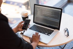 Man working on laptop with phone in hand DevOps.